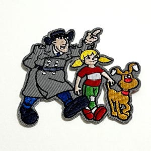 Peut inclure: Écusson brodé représentant des personnages de dessins animés : un homme en imperméable gris, une fille en chemise rouge et pantalon vert, et un chien beige. L'homme pointe, la fille se tient debout et le chien regarde devant lui. L'écusson a une bordure grise.