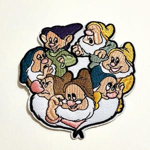 May include: Embroidered patch featuring the seven dwarfs from Snow White. The patch has a white border and depicts the dwarfs in various colors, including green, yellow, brown, and purple. The patch is likely for clothing or accessories.