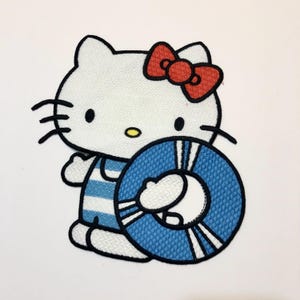 May include: White Hello Kitty cartoon character with a red bow, wearing a blue and white striped swimsuit and holding a blue and white life preserver.