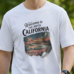 Könnte beinhalten: Weißes T-Shirt mit einem Aufdruck eines roten Cabrios auf einer Straße, die zu einem Hotel bei Sonnenuntergang führt. Der Text "Welcome to THE HOTEL CALIFORNIA" ist über dem Bild aufgedruckt. Das T-Shirt ist aus weichem, bequemem Material.