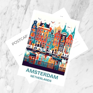 May include: A white postcard with a colourful illustration of Amsterdam canal houses, with the city name and country printed below. The word "POSTCARD" is printed on a second postcard. The background is marble.