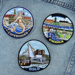 May include: Three embroidered patches featuring cityscapes. One patch depicts a mermaid and the word "Copenhagen". Another shows a river scene with the word "Stockholm". The third patch displays a building and the word "OSLO".