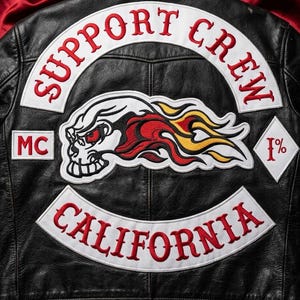 Può includere: Una giacca in pelle nera con grandi toppe ricamate sul retro. La toppa superiore riporta la scritta rossa SUPPORT CREW. Una toppa centrale raffigura un teschio in fiamme con occhi rossi. Le toppe laterali mostrano le scritte MC e 1% e CALIFORNIA.