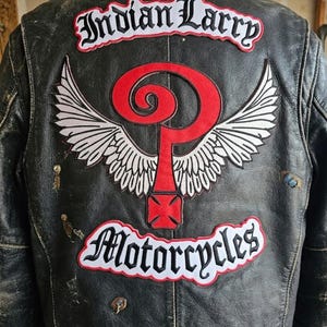 May include: Black leather motorcycle jacket with patches. The patches include the words "Indian Larry" and "Motorcycles" in white script with a red and white winged design. The jacket shows signs of wear.