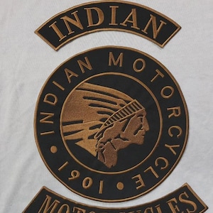 May include: Embroidered patches featuring the "Indian Motorcycles" logo. The patches are black with gold-colored text and a detailed image of a Native American profile. The patches include the words "Indian," "Motorcycles," and the year "1901."
