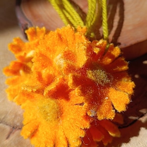 Op de afbeelding: Close-up van een feloranje, pluche bloem met een gele draad. De bloem heeft een getextureerd, gelaagd uiterlijk, met een centrale, iets donkerdere gele kern. De achtergrond is een houten oppervlak.