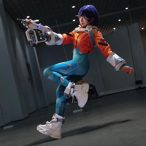 May include: A person with short purple hair wearing a bright orange cropped jacket, teal patterned leggings, and white platform sneakers. They are holding a futuristic white and blue toy blaster with large white gauntlets on their hands.