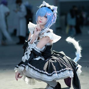 Può includere: Un costume cosplay composto da un abito nero con bordi a balze bianche, un copricapo abbinato con orecchie da gatto e una coda bianca. L'outfit include un fermaglio rosa, maniche bianche con balze e una gonna a strati con motivi floreali.