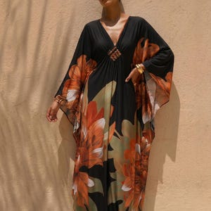 May include: A black floral print maxi dress with a deep V-neckline and wide sleeves. The dress features large orange and white flower designs with green leaves. A decorative embellishment is at the bust.