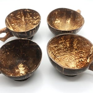 May include: Four handcrafted coconut shell cups with handles. The cups are a natural brown color with a textured interior and a smooth exterior. The handles are also made from coconut shell. These cups are ideal for serving beverages.