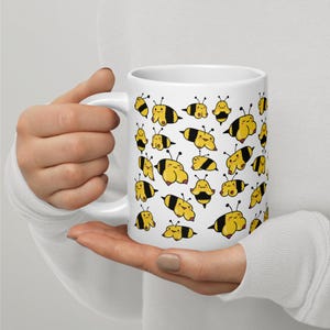 May include: White ceramic mug featuring a repeating pattern of cartoon bees in yellow and black. The bees have a whimsical design, with rounded bodies and small antennae. The mug has a standard handle and a glossy finish.