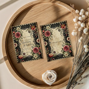 Può includere: Due inviti di nozze in stile vintage con bordi floreali e in pizzo, con i nomi "Matthew & Sarah". Le partecipazioni sono su un vassoio di legno con una rosa bianca e fiori secchi.