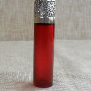 May include: A red glass bottle with a silver, ornate stopper. The bottle is about 6 inches tall and has a round shape.