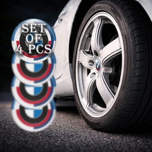 May include: A set of four car wheel centre caps with a blue, red, and white design. The caps are stacked in front of a car wheel and tyre. The text "SET OF 4 PCS" is displayed on the top cap.