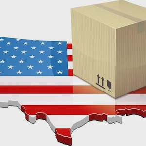 May include: A tan cardboard shipping box with black handling symbols and a barcode, positioned on top of a three-dimensional map of the United States featuring the red, white, and blue stars and stripes flag pattern across its entire surface area.