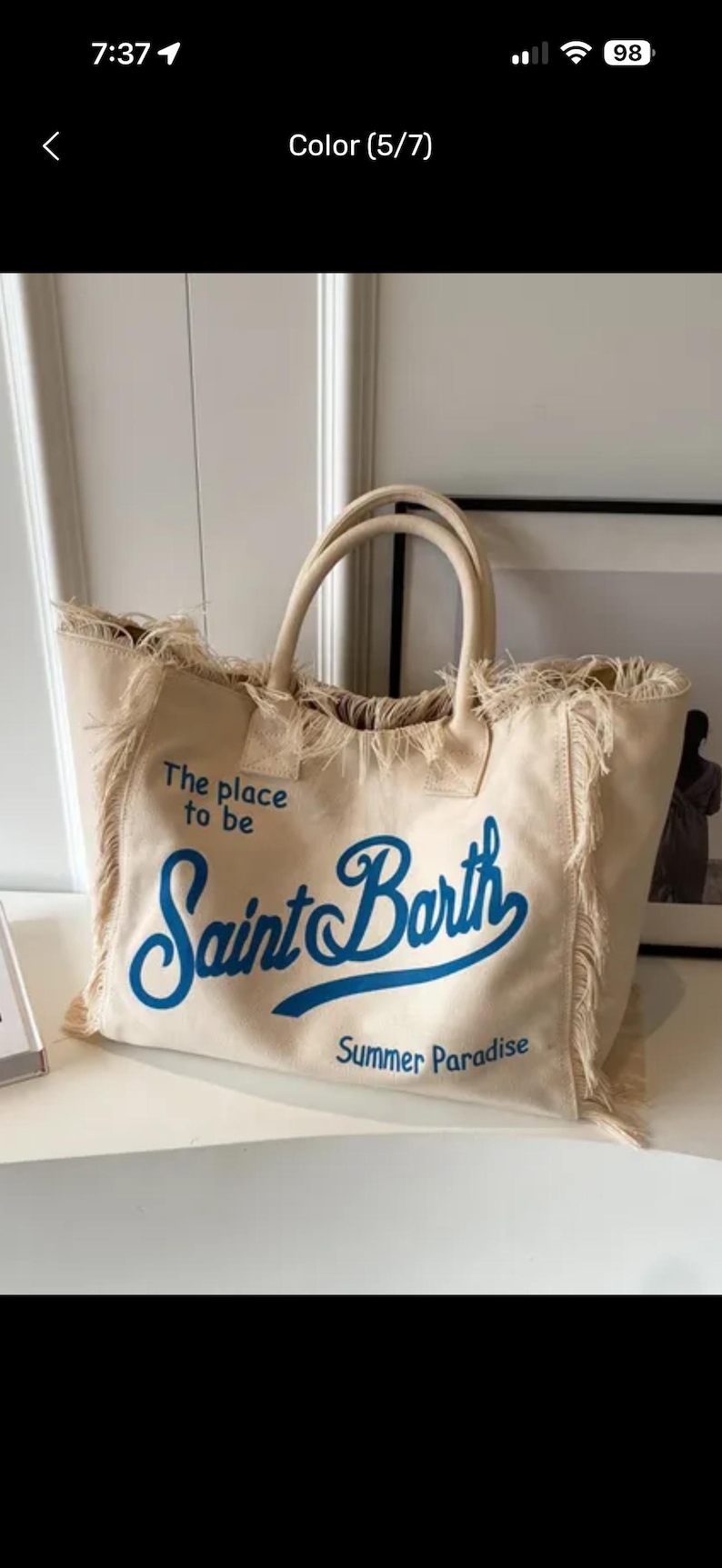 May include: A beige canvas tote bag with two top handles and frayed edges. The bag features blue text that reads The place to be, Saint Barth, and Summer Paradise. The design includes a large script font for the words Saint Barth.