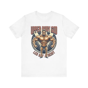 May include: White t-shirt featuring a muscular illustration of a bodybuilder. The design includes the text "UPPER BODY GOD" in red, and "LEG DAY ATHEIST" in a circular design. The shirt is made of a soft, comfortable material.