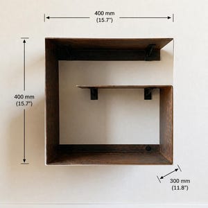 May include: A wooden wall shelf with a square design. The shelf is 15.7 inches high and wide, and 11.8 inches deep. The shelf has a dark brown finish and is mounted on a white wall. The text "Left version" is at the top.