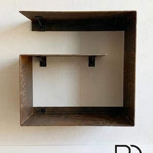 May include: A modern, wall-mounted shelf unit with a dark brown, weathered finish. The design features a large, open square frame with a smaller shelf inside, supported by black metal brackets. The bottom right corner displays the text "RD RUFUS DESIGN Handmade in Italy."