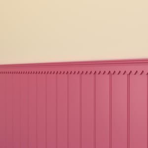 Op de afbeelding: Een gedeelte van een muur met roze lambrisering en een crème-kleurig bovendeel. De lambrisering heeft verticale panelen met een decoratieve bovenrand. Het kleurenpalet is een zachte, uitnodigende combinatie van roze en crème.