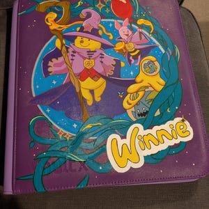 May include: A purple zipped binder featuring a graphic of a yellow bear in a purple wizard hat and cloak holding a wooden staff, a pink piglet with a red balloon, and a yellow honey pot. The text Winnie is printed in yellow on the front.