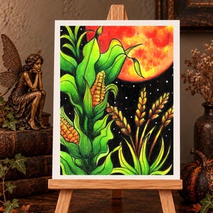Könnte beinhalten: Ein rechteckiger Kunstdruck mit einer lebendigen Illustration von Maispflanzen und Weizen vor einem dunklen Nachthimmel mit einem großen, leuchtend orangefarbenen Mond. Das Kunstwerk zeigt leuchtend grüne Blätter, goldene Maiskolben und Weizenähren vor einem schwarzen Hintergrund mit kleinen weißen Sternen.