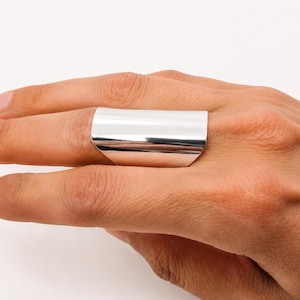 May include: A wide, polished silver-tone ring with a smooth, curved surface that wraps around the finger. The band features a high-shine metallic finish and a broad, flat design that covers a significant portion of the finger's length.