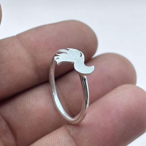 May include: A silver-colored ring featuring a small, flat, stylized squirrel silhouette as the centerpiece. The band is thin and polished, while the squirrel motif has a matte, brushed finish. The metal appears to be a bright, reflective silver tone.