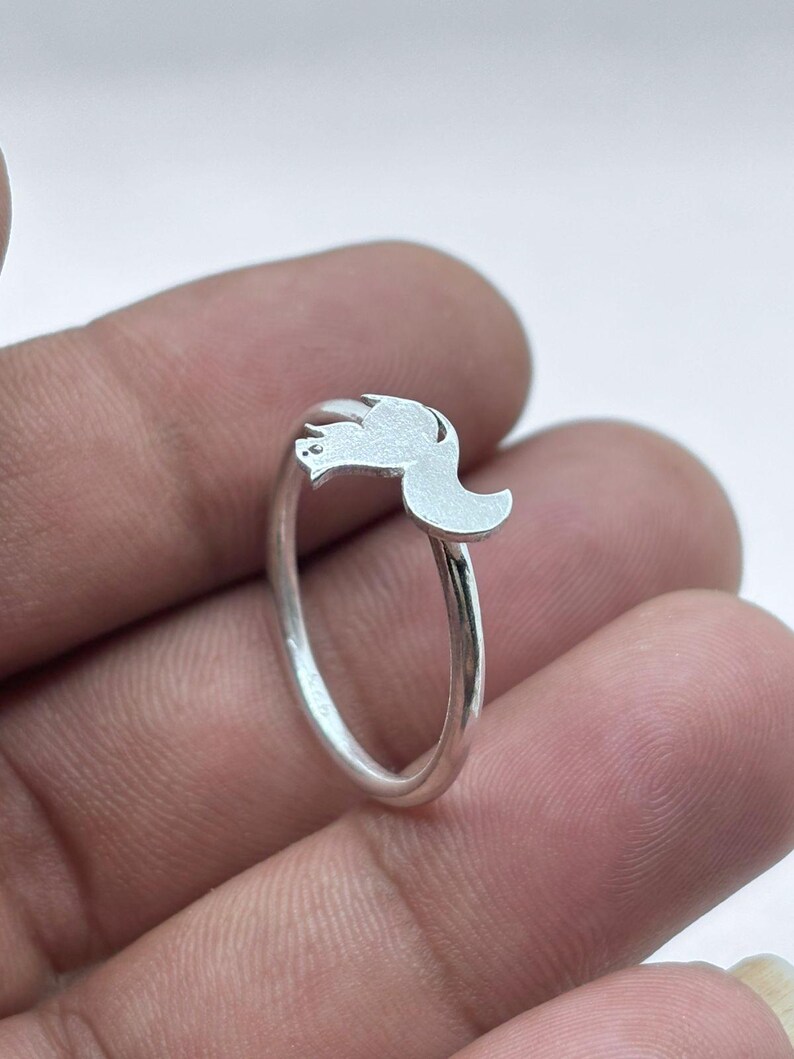 May include: A silver-colored ring featuring a small, flat, stylized squirrel silhouette as the centerpiece. The band is thin and polished, while the squirrel motif has a matte, brushed finish. The metal appears to be a bright, reflective silver tone.