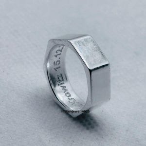 May include: A silver-colored metal ring shaped like a hexagonal nut. The inner band features the engraved text "Krowitz 15.12" and the small text "Indianjewelry925" is visible near the bottom edge of the ring's outer surface.