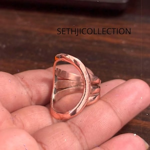 May include: A copper-toned ring featuring a large, open, oval-shaped top section with a smooth, polished finish. The band consists of three distinct, parallel metal strands that converge into the main oval frame. The text SETHJICOLLECTION is visible.