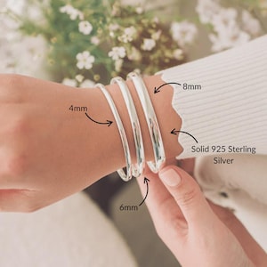 May include: Three solid 925 sterling silver bangle bracelets with smooth, polished surfaces. The bracelets are labelled with widths of 4mm, 6mm, and 8mm. The metal has a bright, reflective finish and a rounded, circular shape for the wrist.