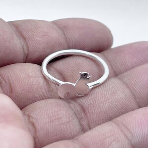 May include: A polished silver ring featuring a small, stylized squirrel silhouette integrated into the band. The metal has a smooth, reflective finish, and the design shows the squirrel in a seated position with its tail curved upward along the ring.