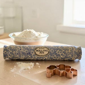 Könnte beinhalten: Eine blau-weiß geblümte Teigrolle mit dem Text "Rolling Pin" wird auf einer Holzoberfläche gezeigt. Ein Kupferausstecher und eine Schüssel mit Mehl sind ebenfalls vorhanden, was auf ein Backthema hindeutet.