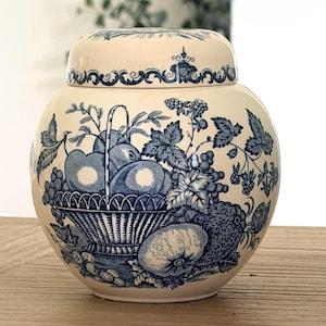May include: A cream-coloured ceramic ginger jar with a matching lid, featuring a blue transferware pattern of a fruit-filled basket, various berries, and leaves. The design includes detailed illustrations of apples, grapes, and brambles.