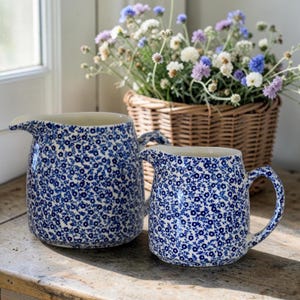 Könnte beinhalten: Eine weiße Keramik-Tasse mit schwarzem Henkel und dem Text "But First, Coffee" in handschriftlichem Stil. Die Tasse steht auf einer weißen Oberfläche. Für Heißgetränke.