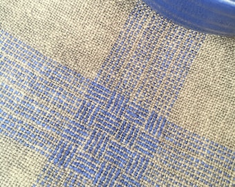 May include: A close-up of a woven linen kitchen towel with a blue and gray geometric pattern. The towel is folded in half and has a blue bowl on top of it.