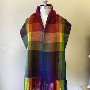 May include: A woven rainbow plaid scarf with fringe. The scarf is made of a variety of colors, including red, orange, yellow, green, blue, and purple.