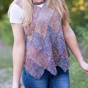 May include: A woman wearing a white t-shirt and blue jeans with a multi-colored knitted vest. The vest has a chevron pattern and is made with a variety of yarns.