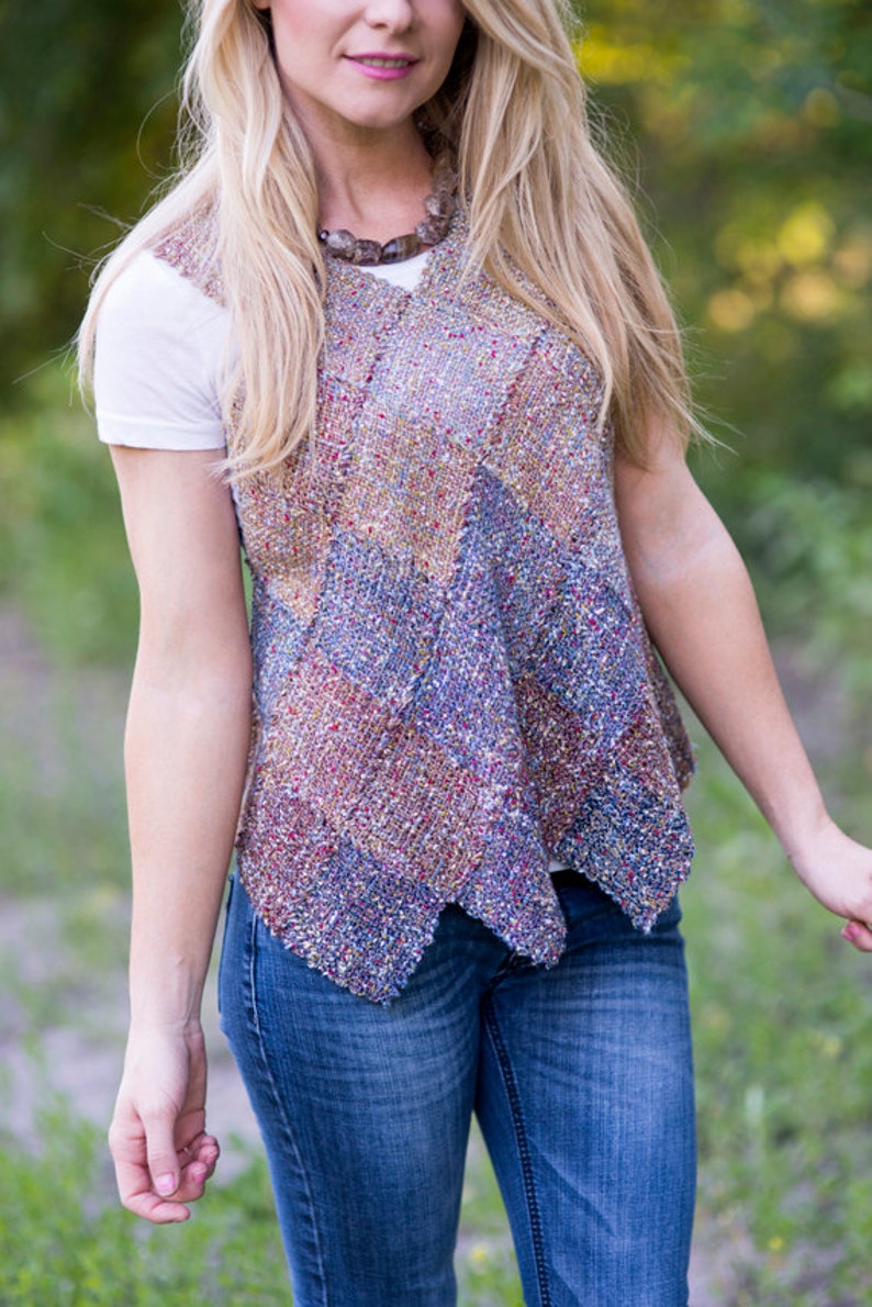 May include: A woman wearing a white t-shirt and blue jeans with a multi-colored knitted vest. The vest has a chevron pattern and is made with a variety of yarns.