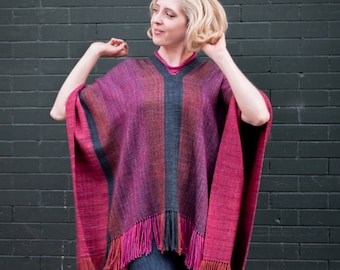 May include: A woman wearing a purple, red, and black striped poncho with fringe. The poncho is woven and has a V-neck.