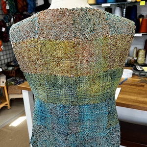 May include: A woven vest with a multi-colored pattern of blue, green, yellow, and brown. The vest is made of a textured fabric and has a slightly frayed edge.