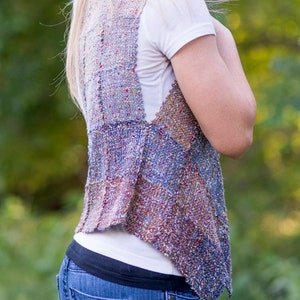 May include: A woman wearing a multi-colored woven vest with a white t-shirt and blue jeans.