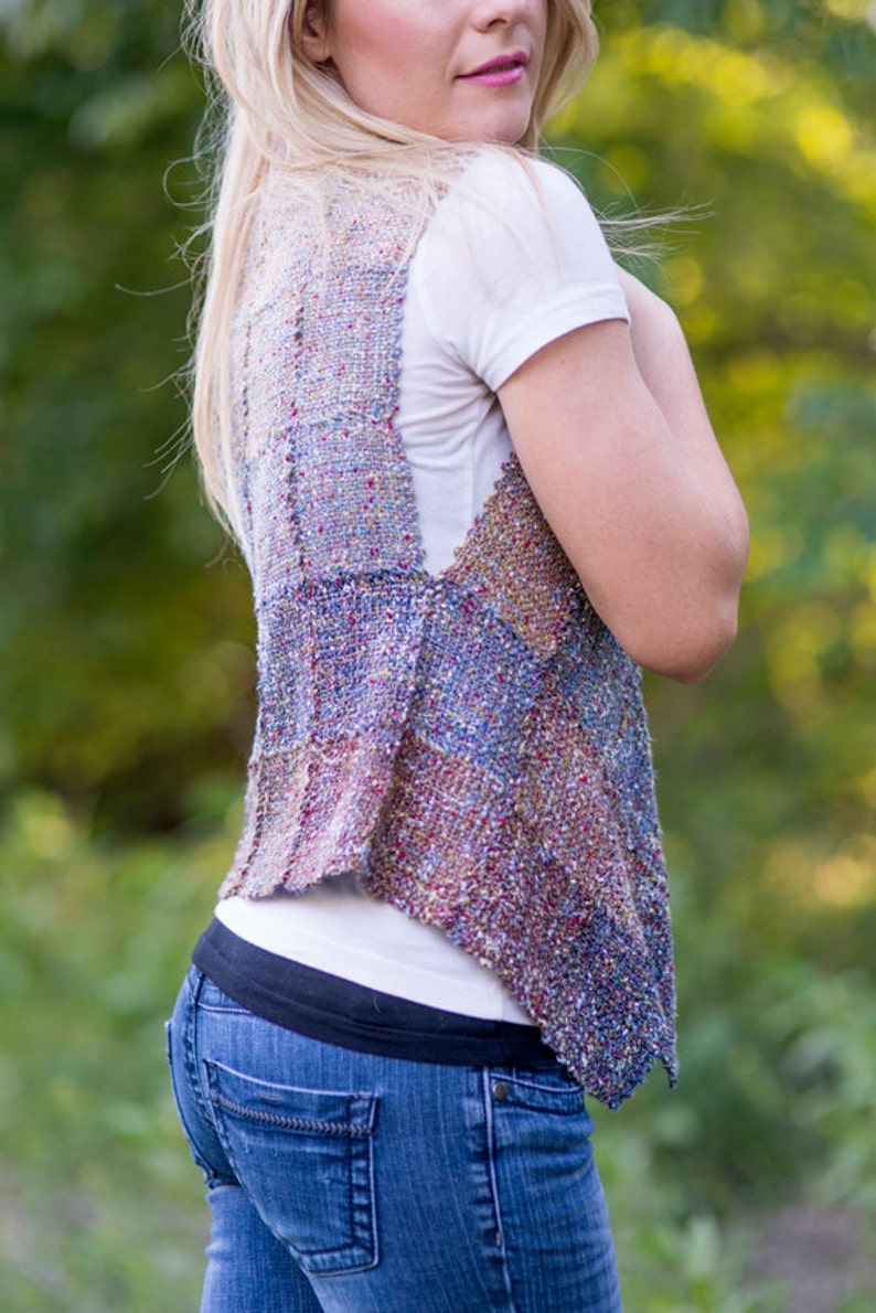 May include: A woman wearing a multi-colored woven vest with a white t-shirt and blue jeans.