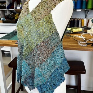 May include: A sleeveless, handwoven top with a V-neckline. The top is made of a variety of colors, including green, blue, and brown. The top is displayed on a white dress form.