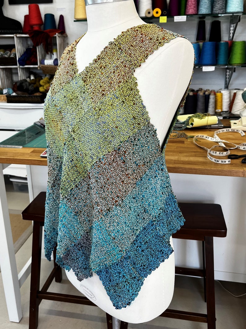 May include: A sleeveless, handwoven top with a V-neckline. The top is made of a variety of colors, including green, blue, and brown. The top is displayed on a white dress form.