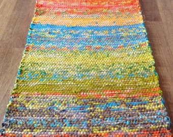 May include: A colourful woven rug with a rainbow pattern and orange fringe. The rug is made from recycled materials and is ideal for adding a splash of colour to any room.