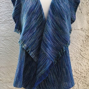 May include: A blue and green woven vest with a fringed hem. The vest has a V-neck and is sleeveless.