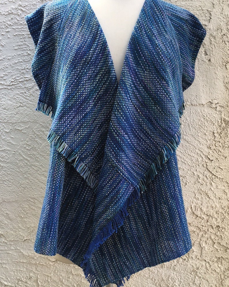 May include: A blue and green woven vest with a fringed hem. The vest has a V-neck and is sleeveless.