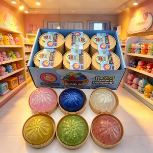 Puede incluir: Una exhibición de juguetes The Original Viral Mystery Dumpling. La caja de exhibición contiene seis cestas de vapor de bambú. Debajo hay seis bolas de masa hervida esféricas de colores en recipientes redondos individuales. Las bolas de masa son rosas, azules, blancas, amarillas, verdes y rojas.